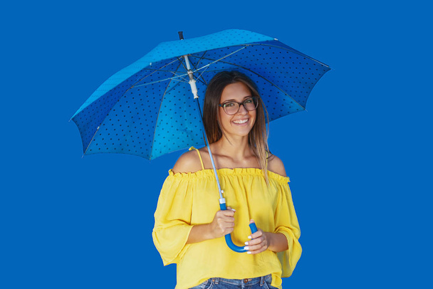 青い傘でポーズ黄色のブラウスで美しい笑顔白人十代の女の子. - 写真・画像