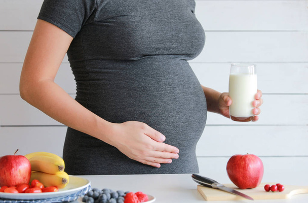 беременная женщина пьет стакан свежего молока со свежими фруктами на столе
 - Фото, изображение