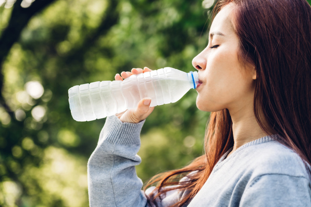 Hermosa mujer asia beber agua de una botella mientras se relaja
 - Foto, Imagen