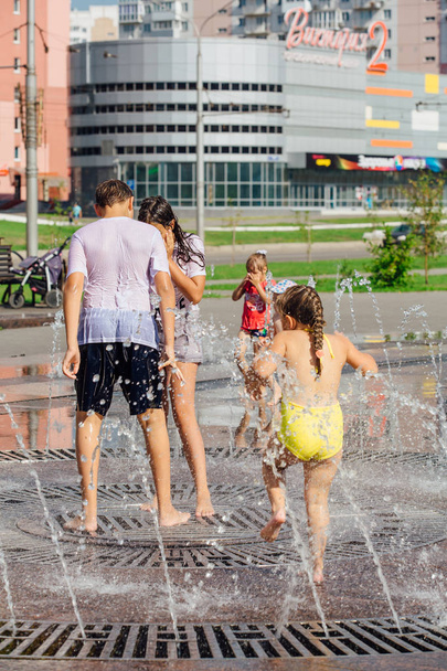 Novokuznetsk, Kemerovo Region, Russia - August 04, 2018: Happy teenagers splashing in a water of a city fountain and enjoying the cool streams of water in a hot day. - Photo, image