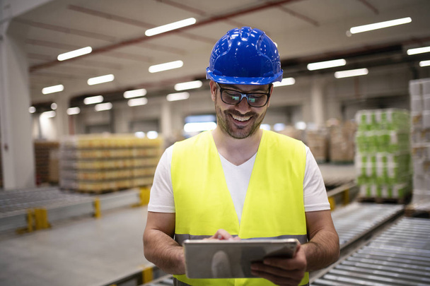 Travailleur de l'industrie dans une veste réfléchissante et un casque rigide regardant la tablette dans l'intérieur de l'usine moderne
. - Photo, image