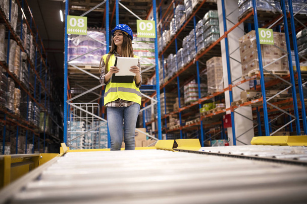 Beautiful woman worker with hardhat and checklist controlling distribution in warehouse center. - Photo, Image