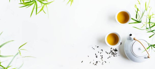 Two white cups of tea and teapot surrounded with green leaves on white background - Foto, imagen