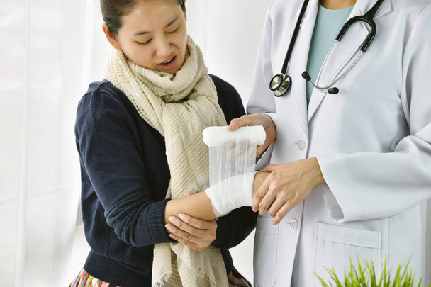 Wypadek urazu ręka, Asian kobieta lekarz z stetoskop bandażowanie rękę pacjenta w szpitalu, Kobieta Twarz pacjenta wyrazić jak bolesne na jej sztywny nadgarstek. - Zdjęcie, obraz