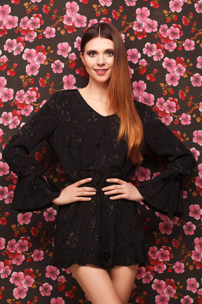Portrait of a beautiful woman in a black dress. Background from a fabric in drawing flowers - Fotoğraf, Görsel