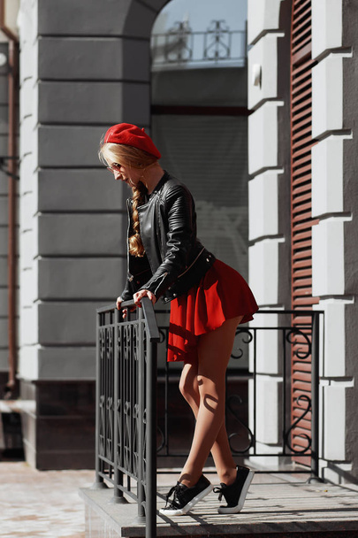 Porträt der schönen jungen blonden Frau in stylischem schwarzen Outfit, sie lächelt auf städtischem Hintergrund - Foto, Bild