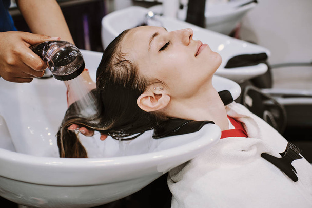 conceito de beleza e pessoas - mulher jovem feliz com cabeleireiro cabeça de lavagem no salão de cabeleireiro
 - Foto, Imagem