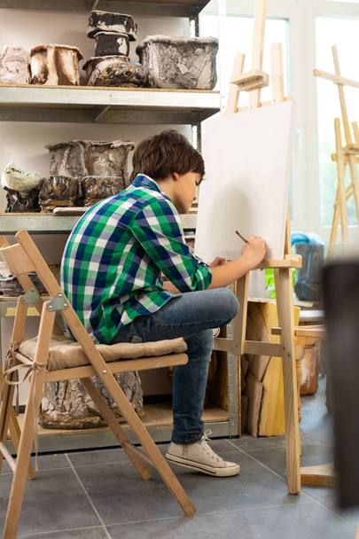 Boy wearing jeans feeling busy while drawing in art school - Photo, Image