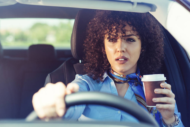 Happy young woman with coffee to go driving her car  - 写真・画像