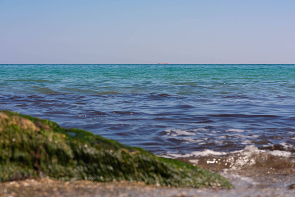 View of the Black Sea on a clear sunny day. On the shore, stones and sand, ships on the horizon. Blue sky and beautiful clouds. - Photo, Image