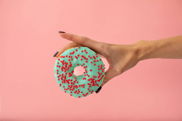 Hand with donut on pink background - Foto, afbeelding