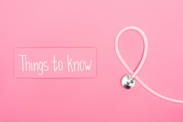Draufsicht auf Stethoskop und rosa Karte mit Wissenswertem Slogan auf rosa Hintergrund - Foto, Bild