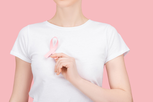 частичный вид женщины в белой футболке, держащей розовый знак рака молочной железы изолирован на розовый
 - Фото, изображение