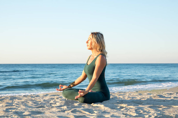 Kaukasische gezonde vrouw met mooi lichaam doen yoga bij zonsopgang op het strand, yoga poses - Foto, afbeelding