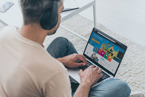 KYIV, UKRAINE - MAY 5, 2019: Man in headphones sitting on floor and using laptop with Amazon app on screen. - Фото, зображення