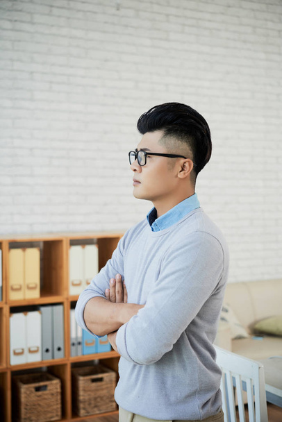 Side näkymä komea aasialainen mies tyylikäs lasit pitää kädet ristissä seistessään mukava toimisto
 - Valokuva, kuva