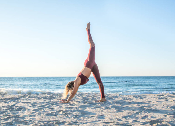 Kaukasische gezonde volwassen vrouw met mooi lichaam doen yoga bij zonsopgang op het strand, yoga poses - Foto, afbeelding