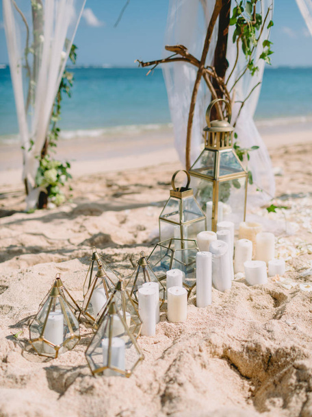 Decoraties van de bruiloft boog met witte bloemen en kaarsen op het strand - Foto, afbeelding