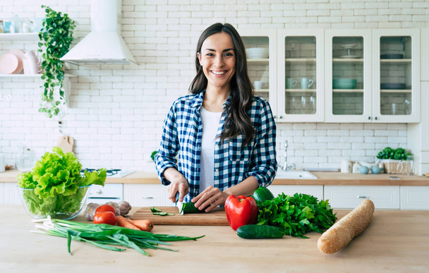 Beautiful young woman is preparing vegetable salad in the kitchen. Healthy Food. Vegan Salad. Diet. Dieting Concept. Healthy Lifestyle. Cooking At Home. Prepare Food. Cutting ingredients on table - Foto, immagini