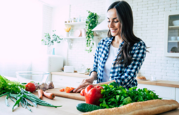 Beautiful young woman is preparing vegetable salad in the kitchen. Healthy Food. Vegan Salad. Diet. Dieting Concept. Healthy Lifestyle. Cooking At Home. Prepare Food. Cutting ingredients on table - Фото, зображення