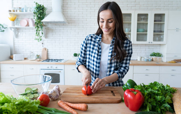 Beautiful young woman is preparing vegetable salad in the kitchen. Healthy Food. Vegan Salad. Diet. Dieting Concept. Healthy Lifestyle. Cooking At Home. Prepare Food. Cutting ingredients on table - Foto, Bild