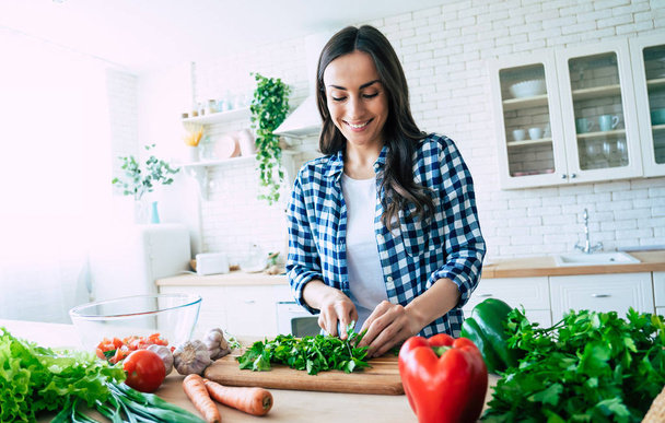 Beautiful young woman is preparing vegetable salad in the kitchen. Healthy Food. Vegan Salad. Diet. Dieting Concept. Healthy Lifestyle. Cooking At Home. Prepare Food. Cutting ingredients on table - Foto, Imagen