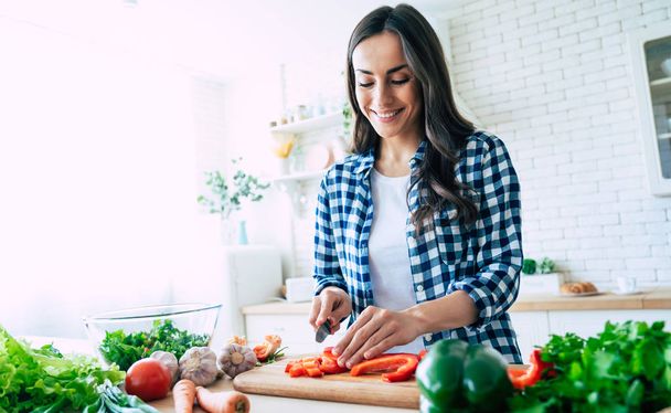 Beautiful young woman is preparing vegetable salad in the kitchen. Healthy Food. Vegan Salad. Diet. Dieting Concept. Healthy Lifestyle. Cooking At Home. Prepare Food. Cutting ingredients on table - Photo, Image