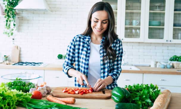 Beautiful young woman is preparing vegetable salad in the kitchen. Healthy Food. Vegan Salad. Diet. Dieting Concept. Healthy Lifestyle. Cooking At Home. Prepare Food. Cutting ingredients on table - Фото, изображение