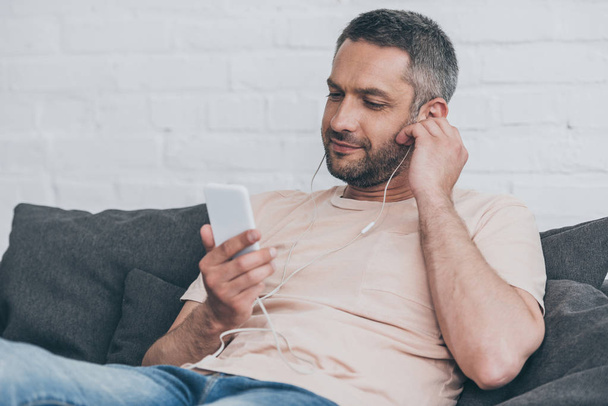 smiling man using smartphone while listening music in earphones - Foto, imagen
