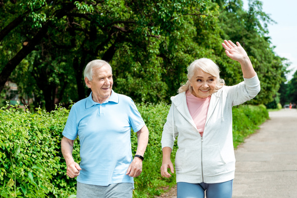 cheerful senior man looking at wife waving hand in park  - Foto, Imagen