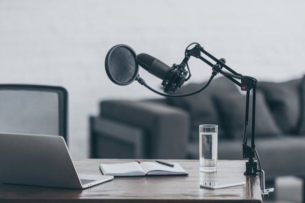 micrófono, portátil, portátil y vaso de agua en la mesa de madera en el estudio de radiodifusión
 - Foto, Imagen