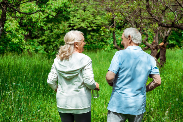 ηλικιωμένη γυναίκα κοιτάζοντας τον σύζυγο, ενώ τρέχουν σε πράσινο πάρκο  - Φωτογραφία, εικόνα