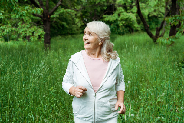 happy senior woman with grey hair running in green park  - Photo, image