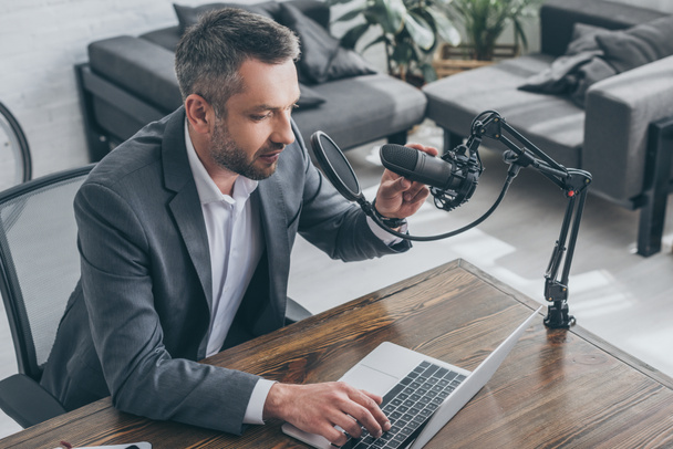 красивый радиоведущий, регулирующий микрофон и использующий ноутбук в студии радио
 - Фото, изображение