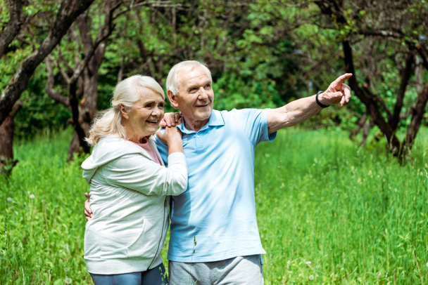 cheerful retired man pointing with finger near happy wife with grey hair - Foto, imagen
