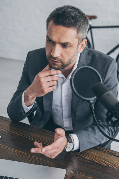 pensive radio host gesturing while speaking in microphone in broadcasting studio - Photo, Image