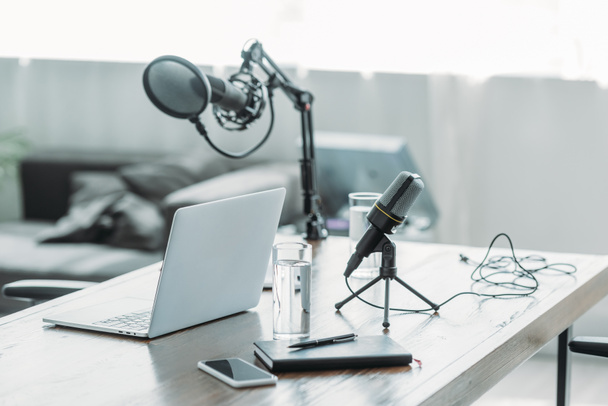 деревянный стол с микрофоном, ноутбуком, смартфоном, ноутбуком и стаканами воды в студии вещания
 - Фото, изображение