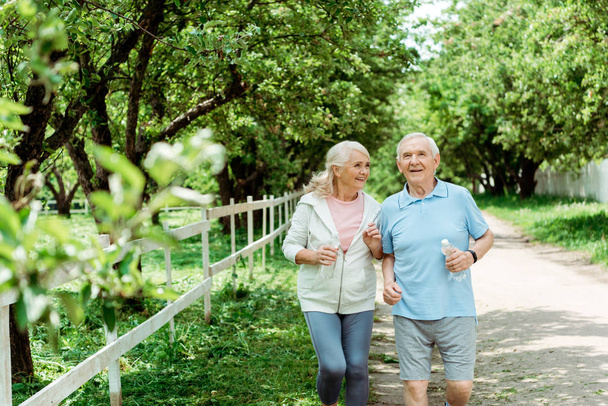 selective focus of cheerful retired man running near senior wife in park  - Foto, afbeelding