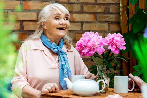 ピンクの花の近くで微笑む幸せな引退した女性の選択的な焦点  - 写真・画像