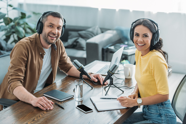 dos alegres anfitriones de radio sonriendo a la cámara mientras están sentados en el lugar de trabajo en el estudio de radiodifusión
 - Foto, imagen