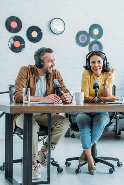 zwei lächelnde Radiomoderatoren sitzen am Arbeitsplatz im Sendestudio und nehmen gemeinsam einen Podcast auf  - Foto, Bild