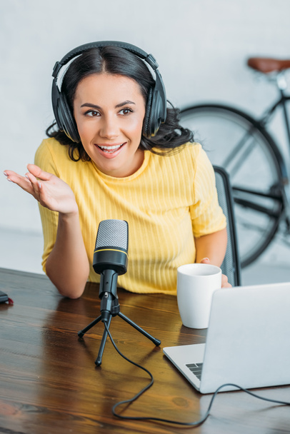 cheerful radio host gesturing while speaking in microphone in studio - Foto, afbeelding