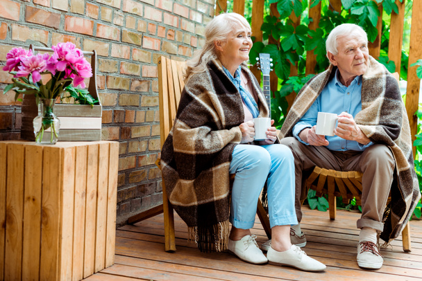 χαρούμενη ηλικιωμένη γυναίκα και τον άνθρωπο που κάθονται στη βεράντα και κρατώντας φλιτζάνια  - Φωτογραφία, εικόνα