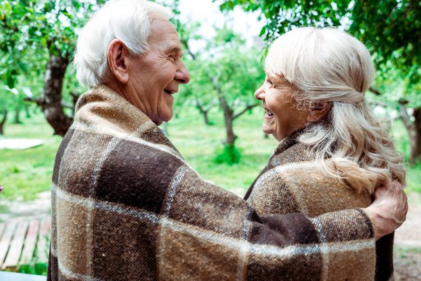 Senior man knuffelen gelukkig gepensioneerde vrouw in geruite deken  - Foto, afbeelding