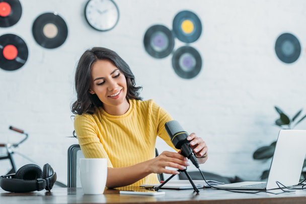 симпатичный радиоведущий регулирует микрофон, сидя на рабочем месте в студии
 - Фото, изображение