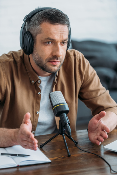 serious radio host gesturing while speaking in microphone in broadcasting studio - Photo, Image
