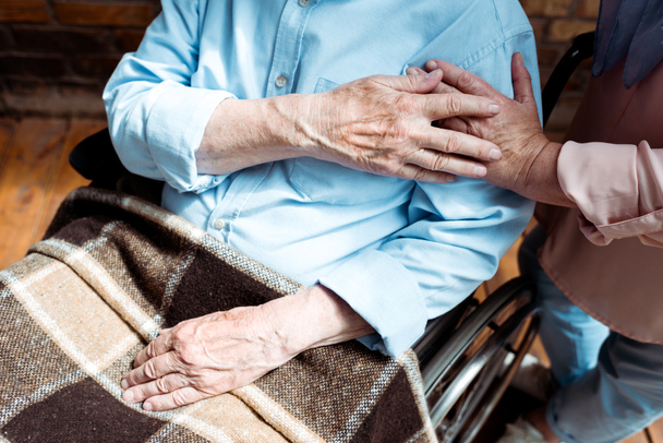 przycięte widok starszy mężczyzna niepełnosprawnych trzymając ręce z żoną  - Zdjęcie, obraz