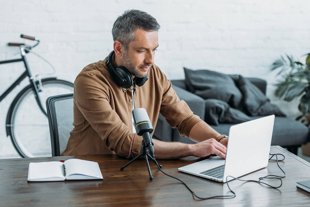 attentive radio host using laptop while sitting at workplace near microphone - Φωτογραφία, εικόνα