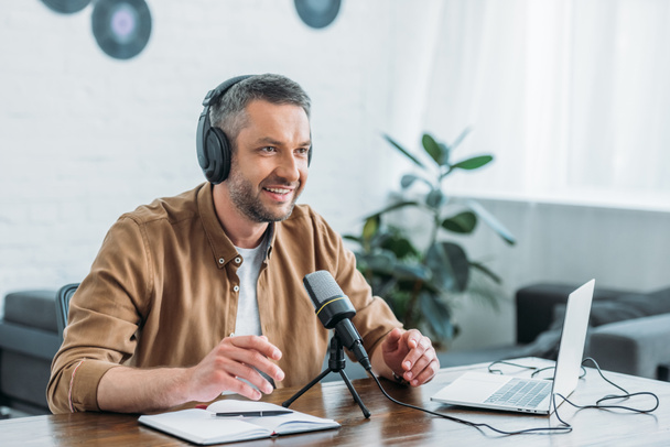 smiling radio host in headphones recording podcast in broadcasting studio - Foto, afbeelding