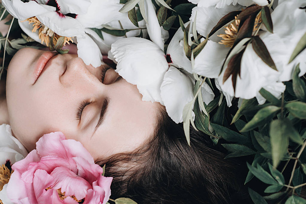 Overhead view of beautiful dreamy young Caucasian woman smiling with closed eyes lying with white flowers. Wellness, travel and people concept. - Foto, Bild